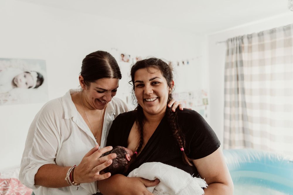 A couple shares joyful moments together while lounging in bed with white linens and natural light streaming in.