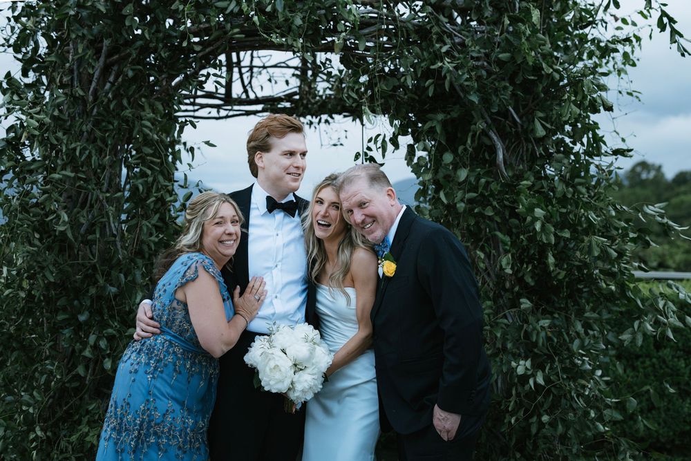 A wedding party poses together under a lush green archway during an outdoor ceremony.