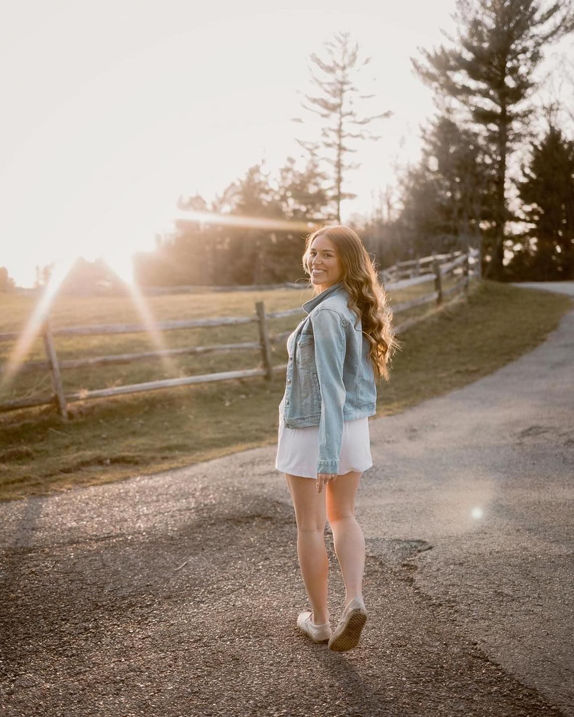 Golden sunset portrait on a rural path with denim jacket and flowing dress.