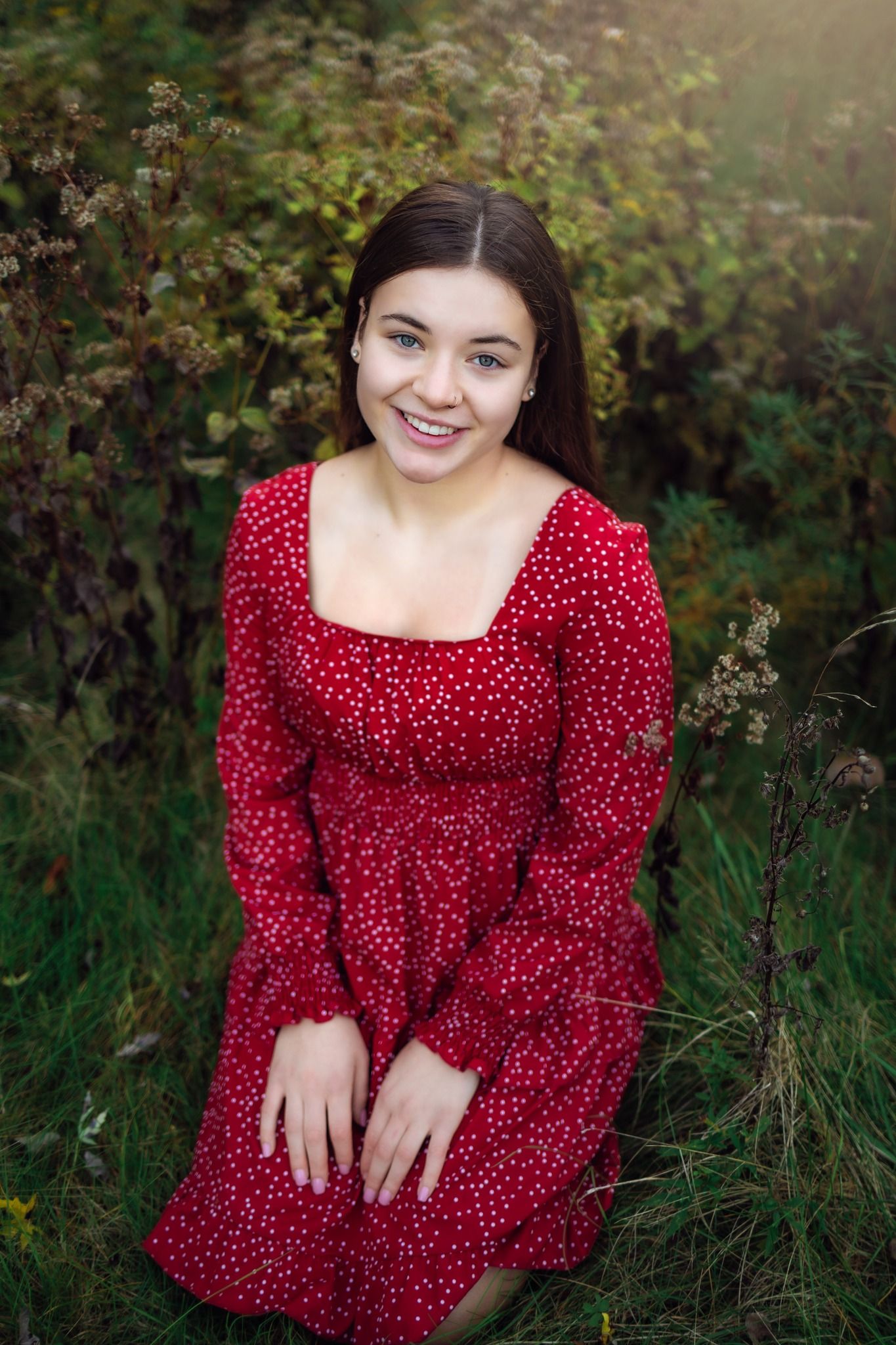 Outdoor portrait in red polka dot dress against green foliage.