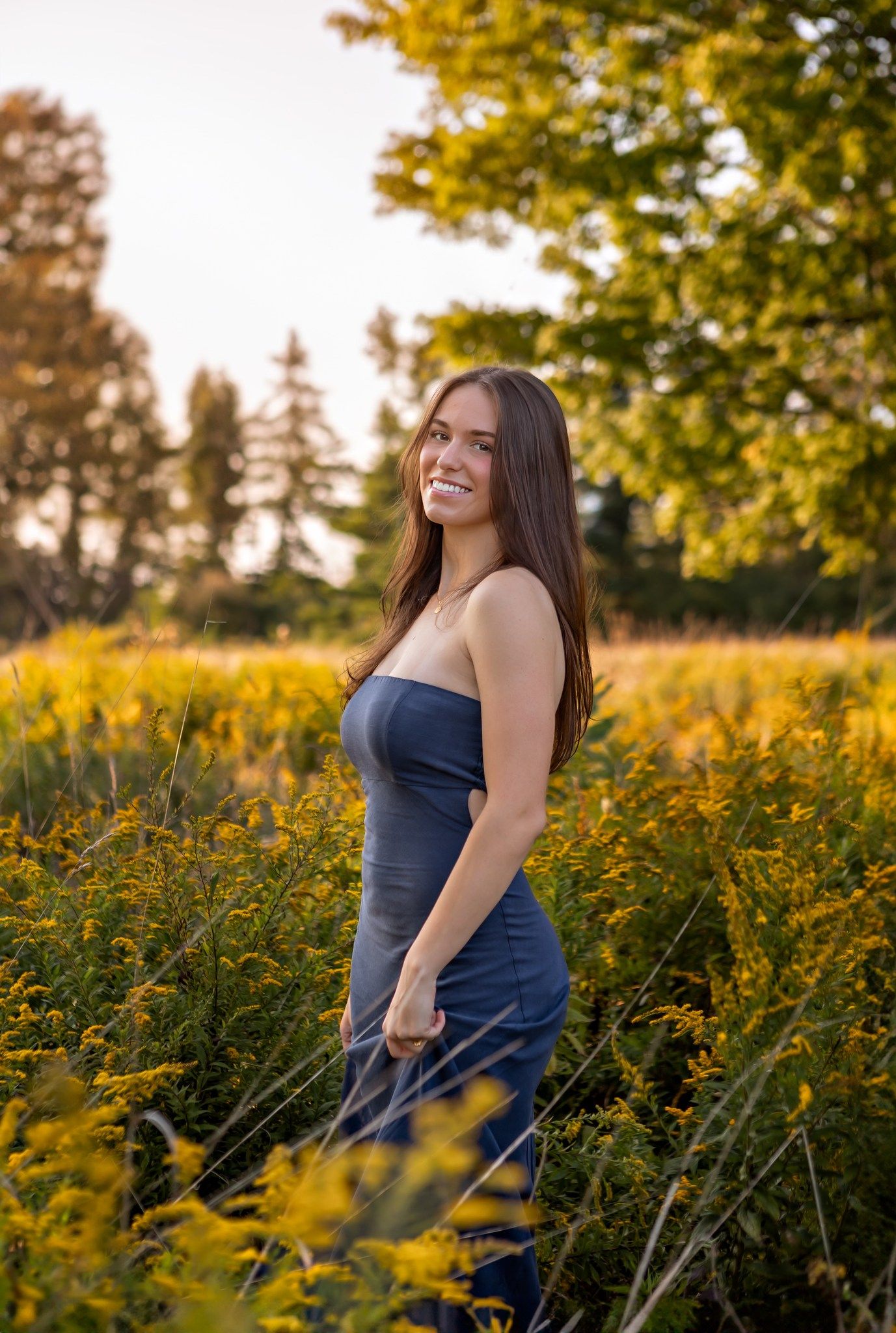 Evening portrait in field of yellow wildflowers wearing navy dress.