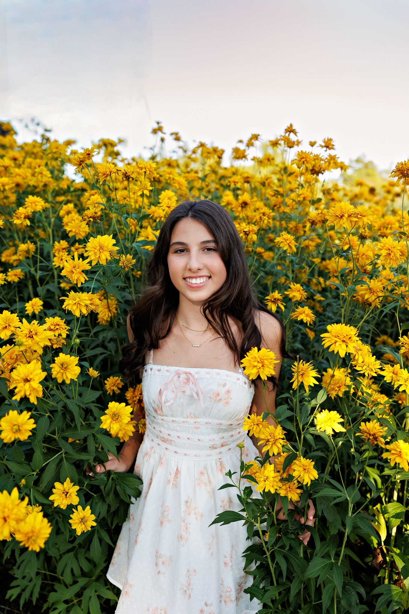 A floral summer portrait in a field of bright yellow flowers with a white floral dress.
