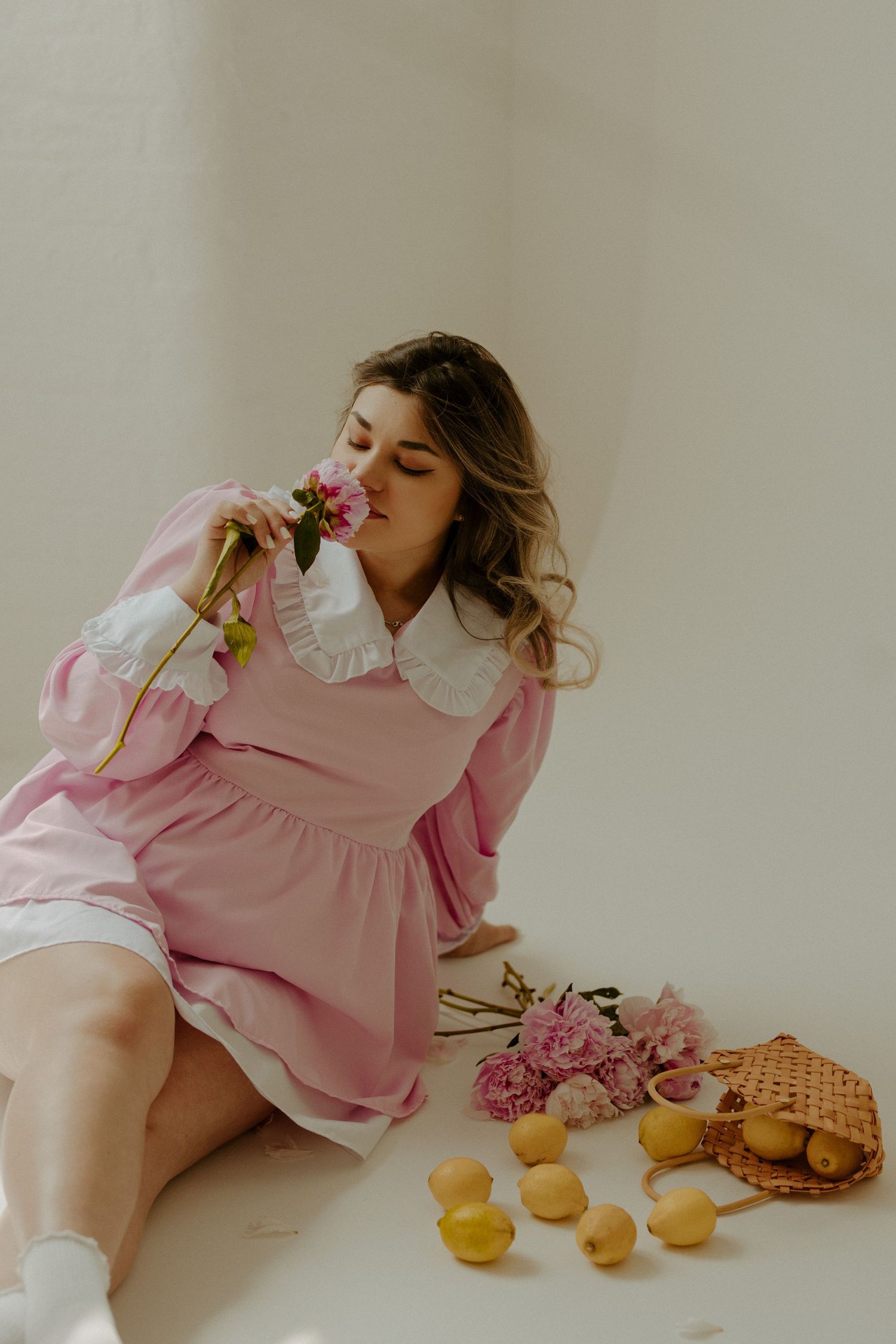 A person in a pink dress lies on a white surface with macarons and flowers arranged in a dreamy, editorial style composition.