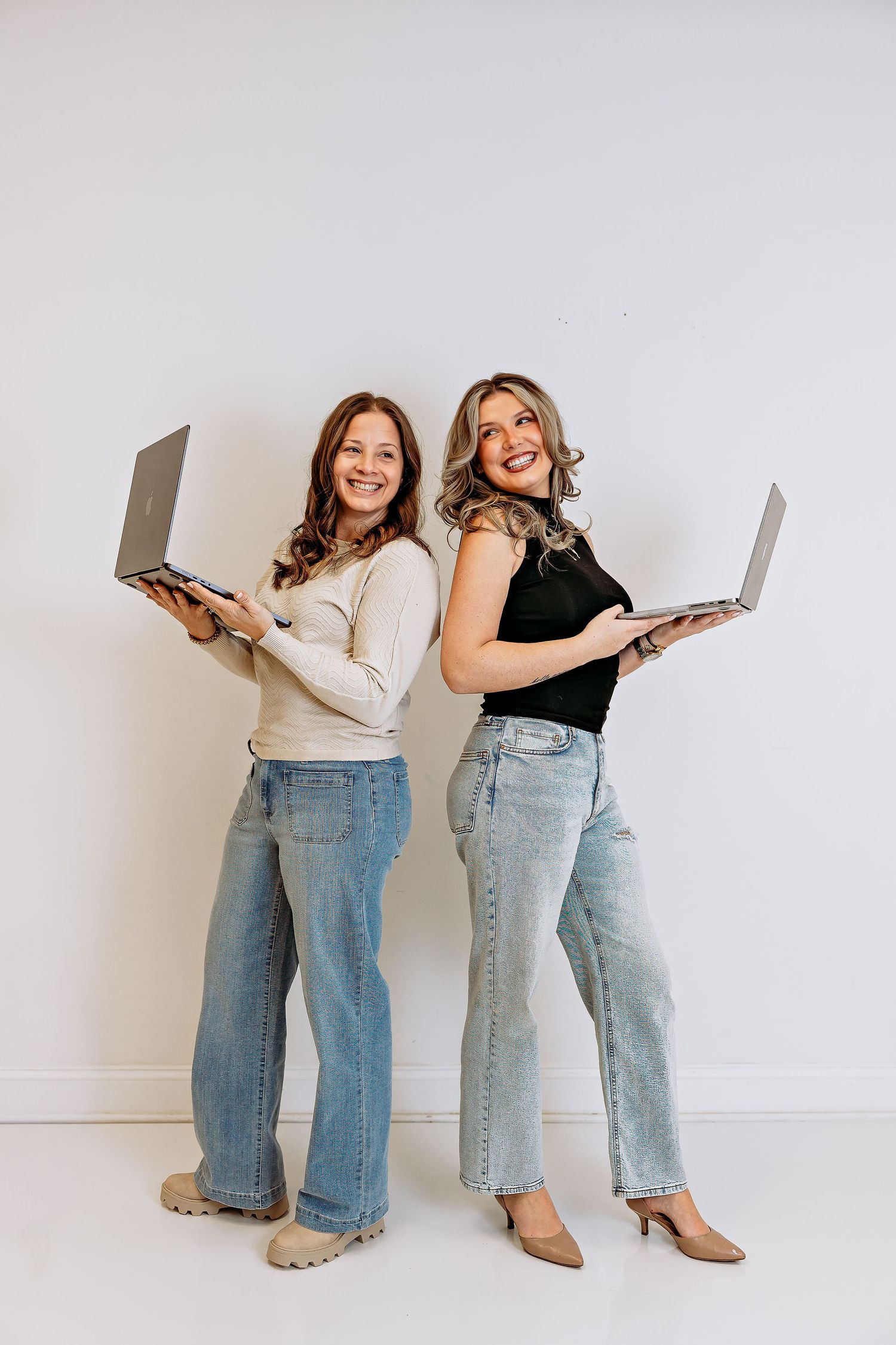 Two people in casual attire holding laptops against white background.