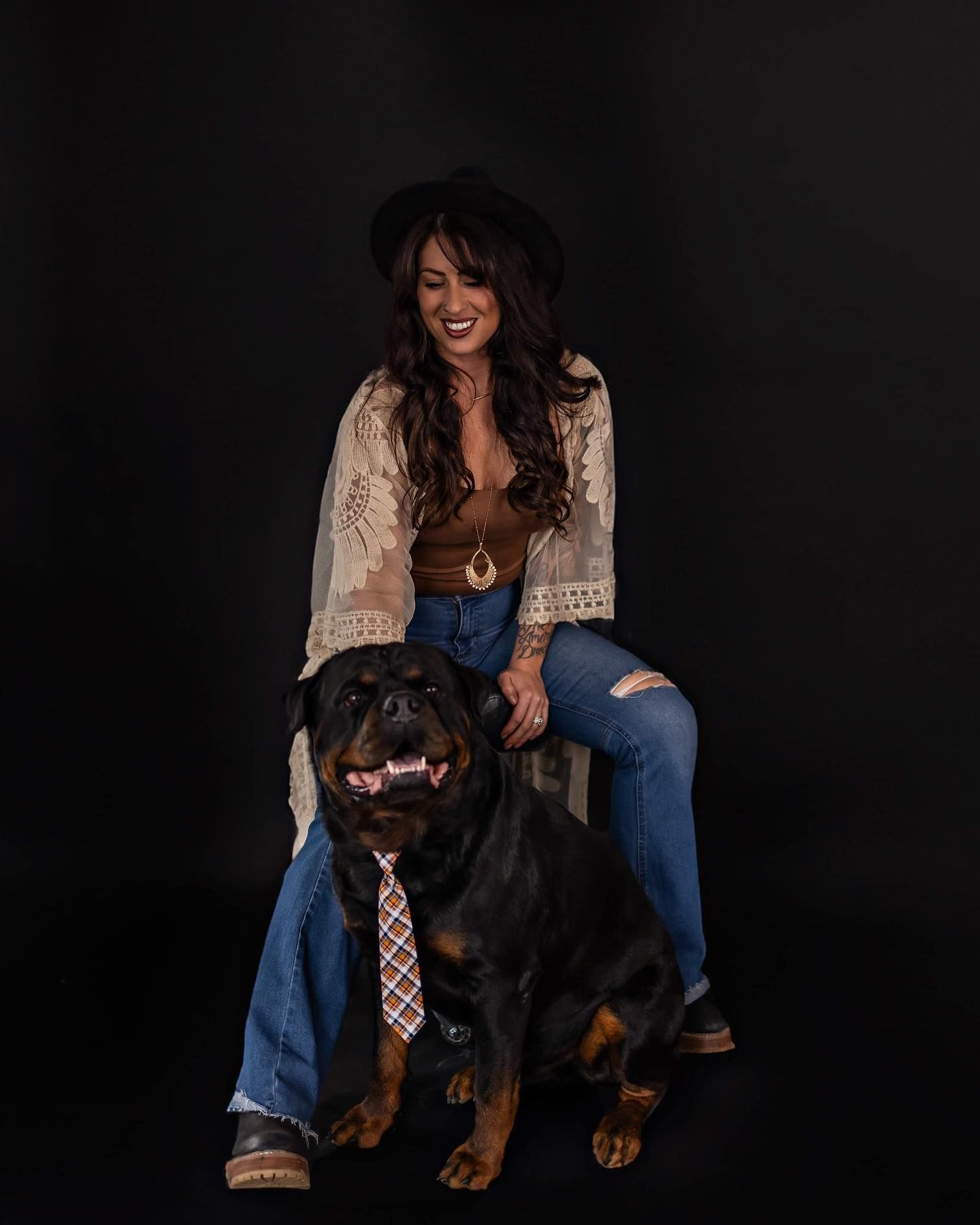 Black dog wearing a tie poses with owner against dark background.