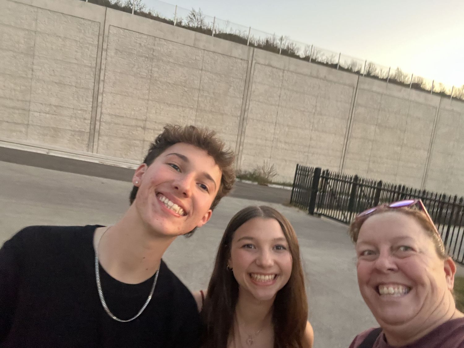 A group of friends taking a series of casual selfies together outdoors against a concrete wall.
