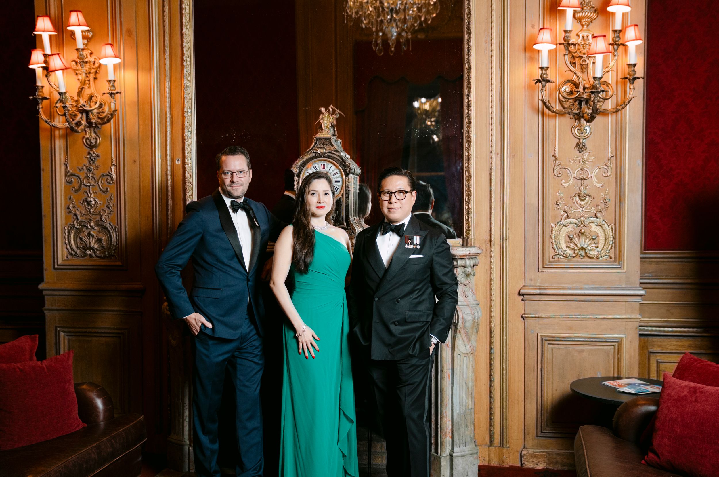 Elegant couple poses in luxurious ballroom setting with ornate chandeliers and wood-paneled walls.