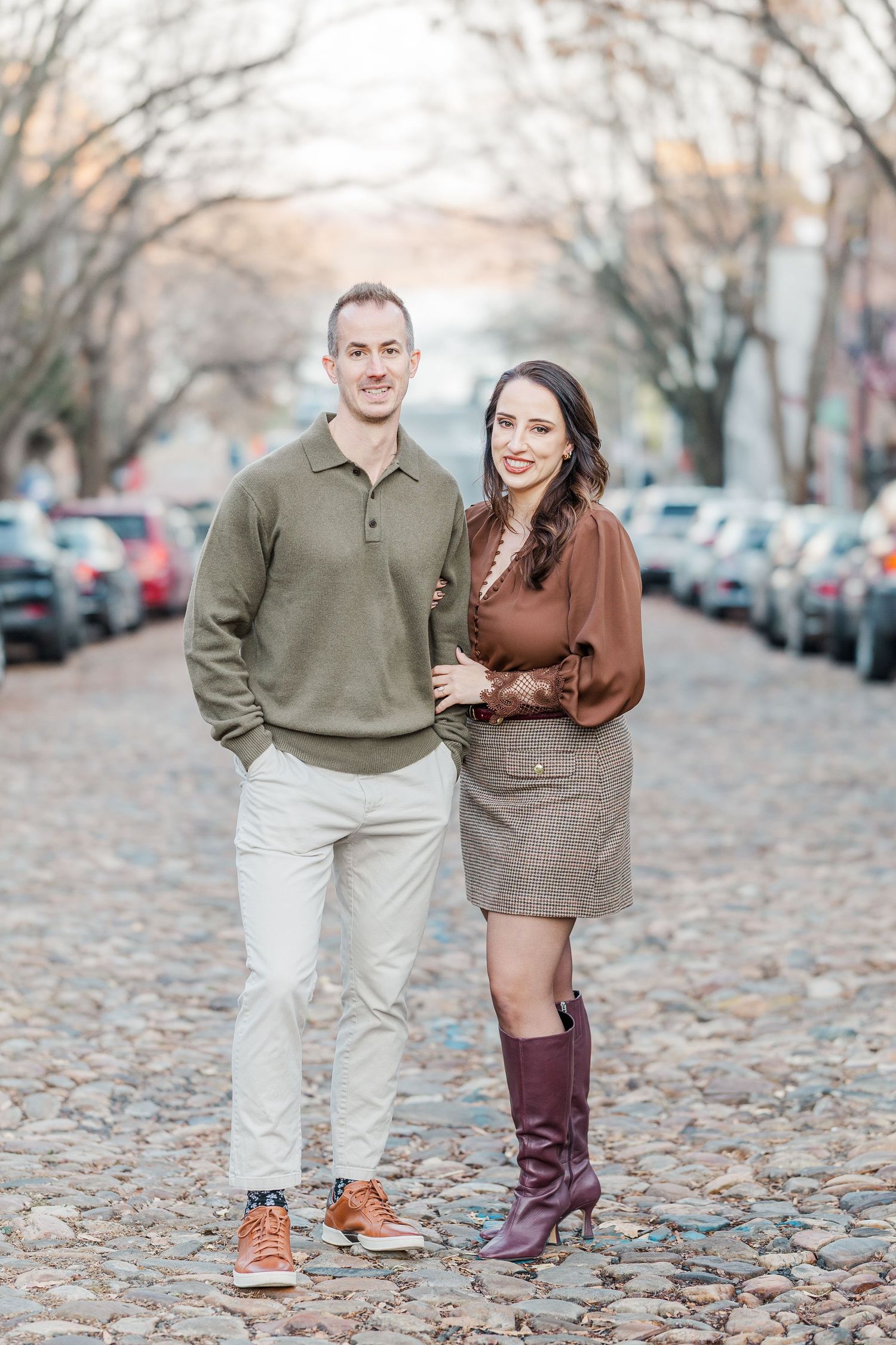 A couple in coordinated fall outfits walks together on a leaf-covered street during autumn.