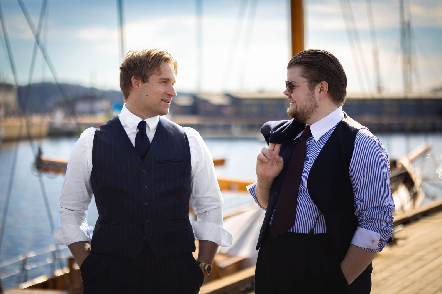 To menn i dress ved havn og båter, bryllupsfoto og groomsmen-portrett av Prospectxmedia Norge.