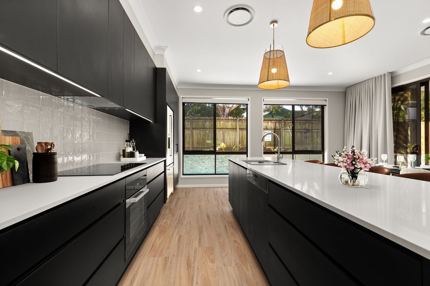 Sleek modern kitchen with black cabinetry, white stone island bench, pendant lights, and garden view window.