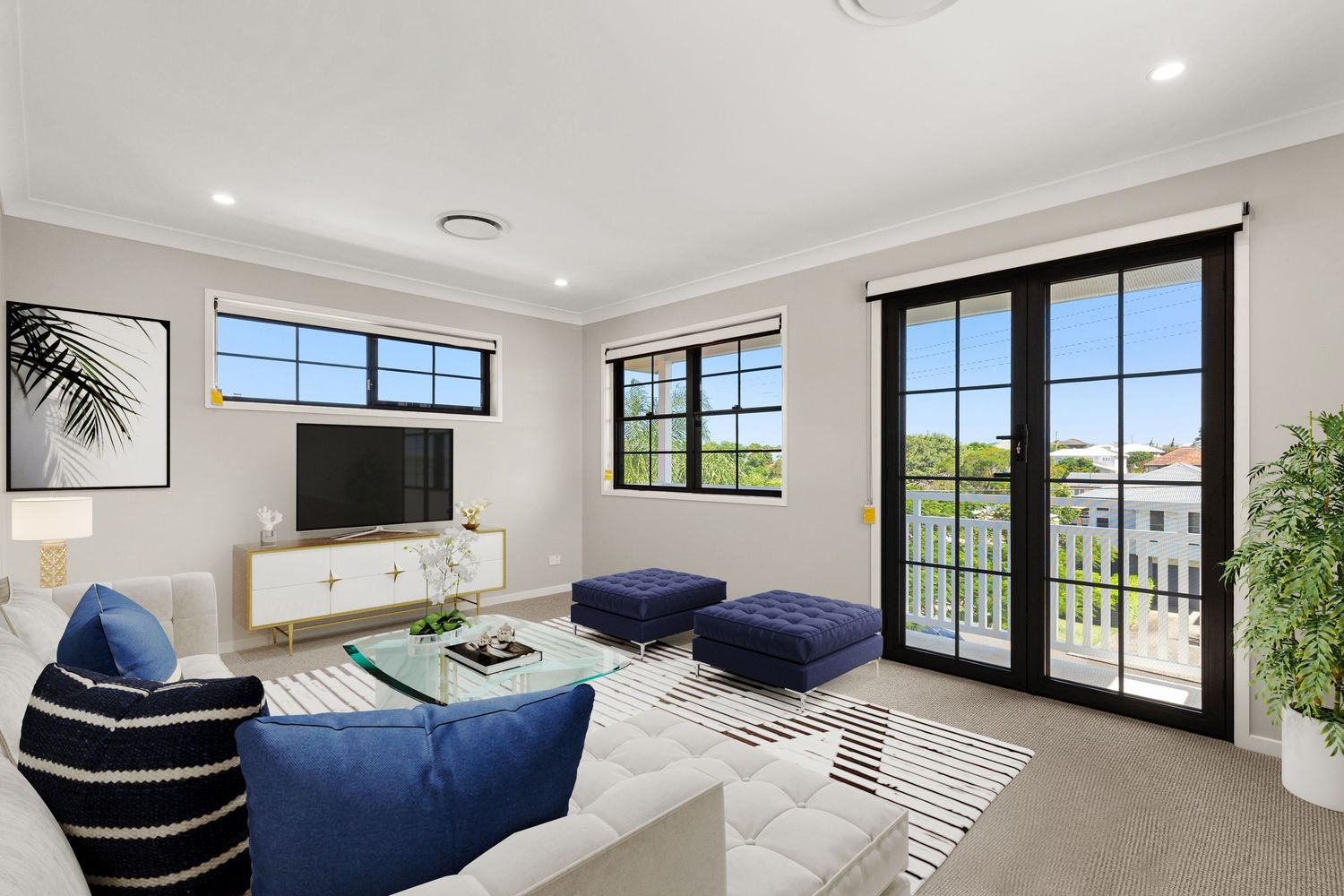 Bright living room with white sofa, blue ottomans, black-framed windows, TV unit, and balcony access in modern home.