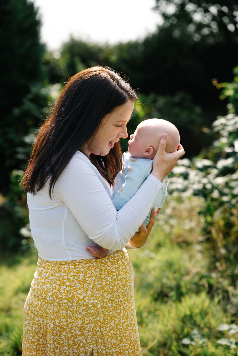 A tender moment between parent and baby in a sunny garden setting with wildflowers and greenery in the background.
