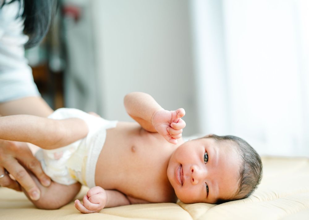 Baby in white cloth lying on soft surface with natural lighting from window.