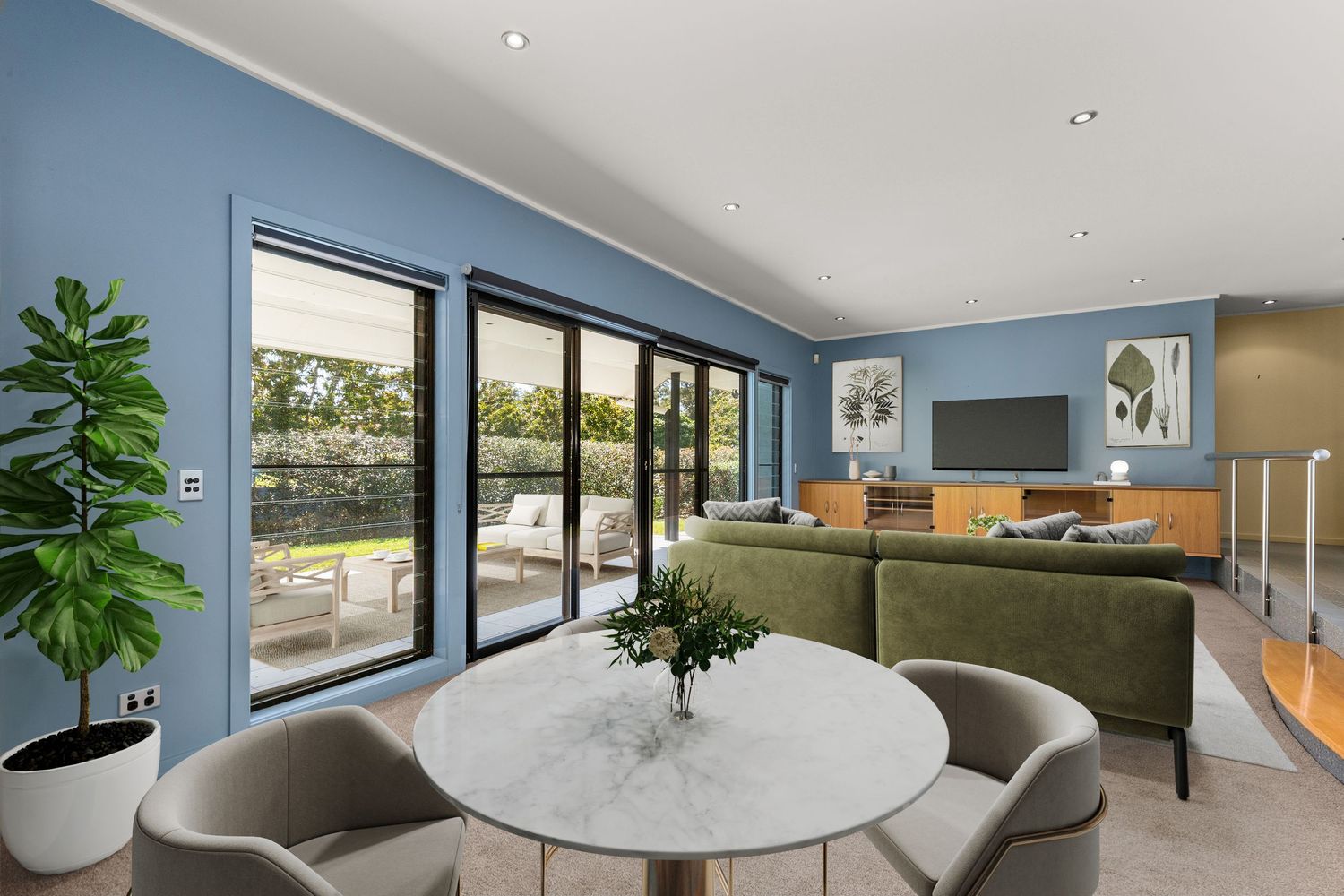 Modern open-plan living and dining area with blue walls, marble table, green sofa, and sliding doors to outdoor patio.