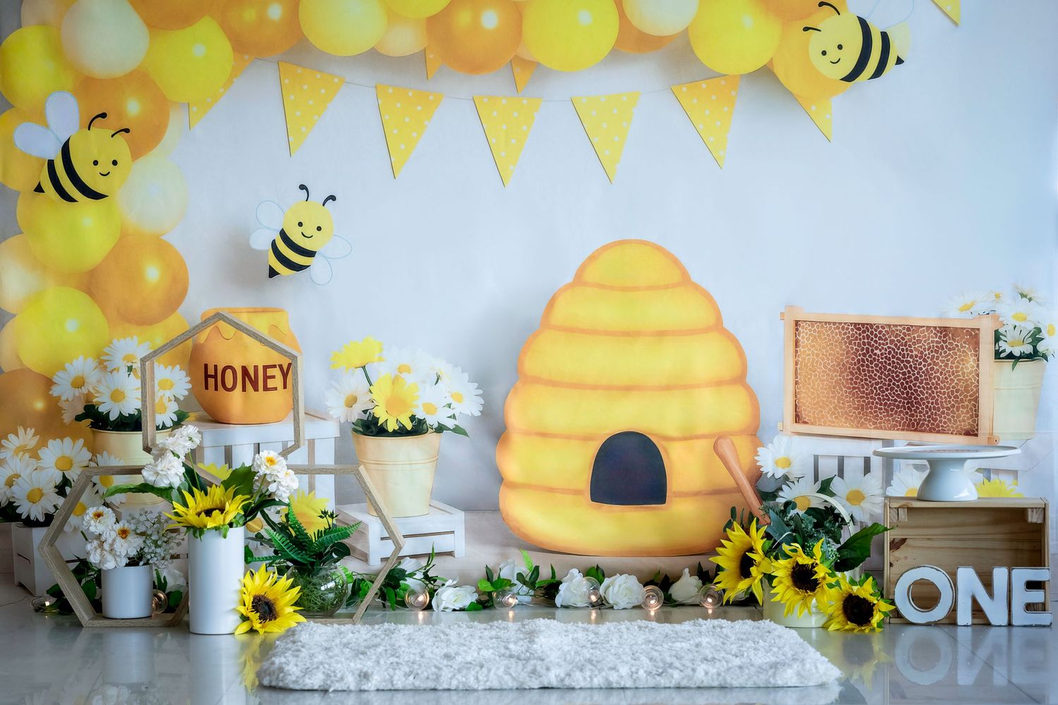 A bee-themed party setup with yellow balloons, honeycomb decorations, sunflowers, and a beehive backdrop for Smash & Splash photography.