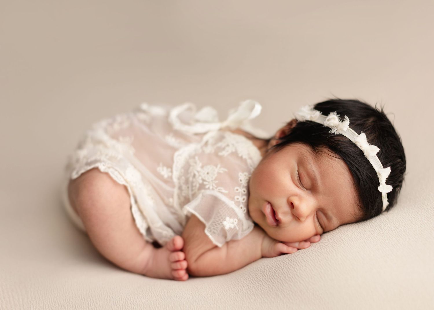 A newborn baby sleeping peacefully in a white woven basket with soft beige fabric backdrop. Elizabeth Lang Photography Surrey
