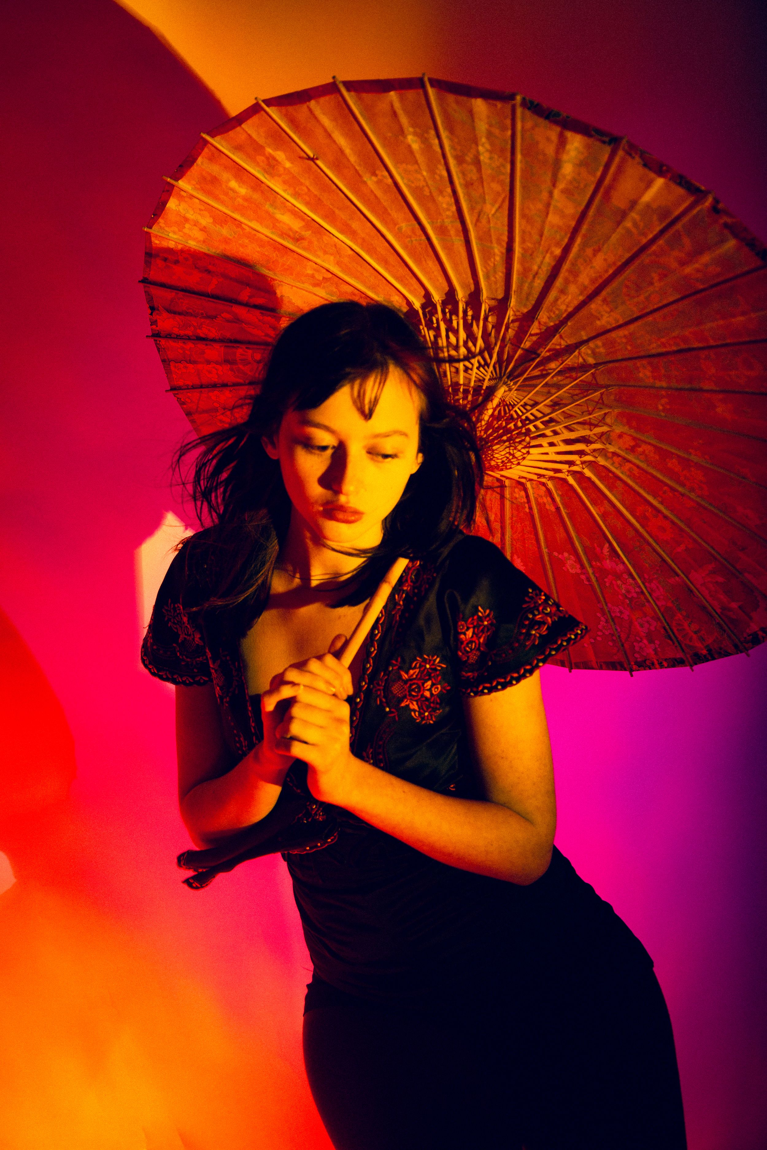 Artistic silhouette portrait with decorative parasol against vibrant red and purple gradient background in dramatic lighting.
