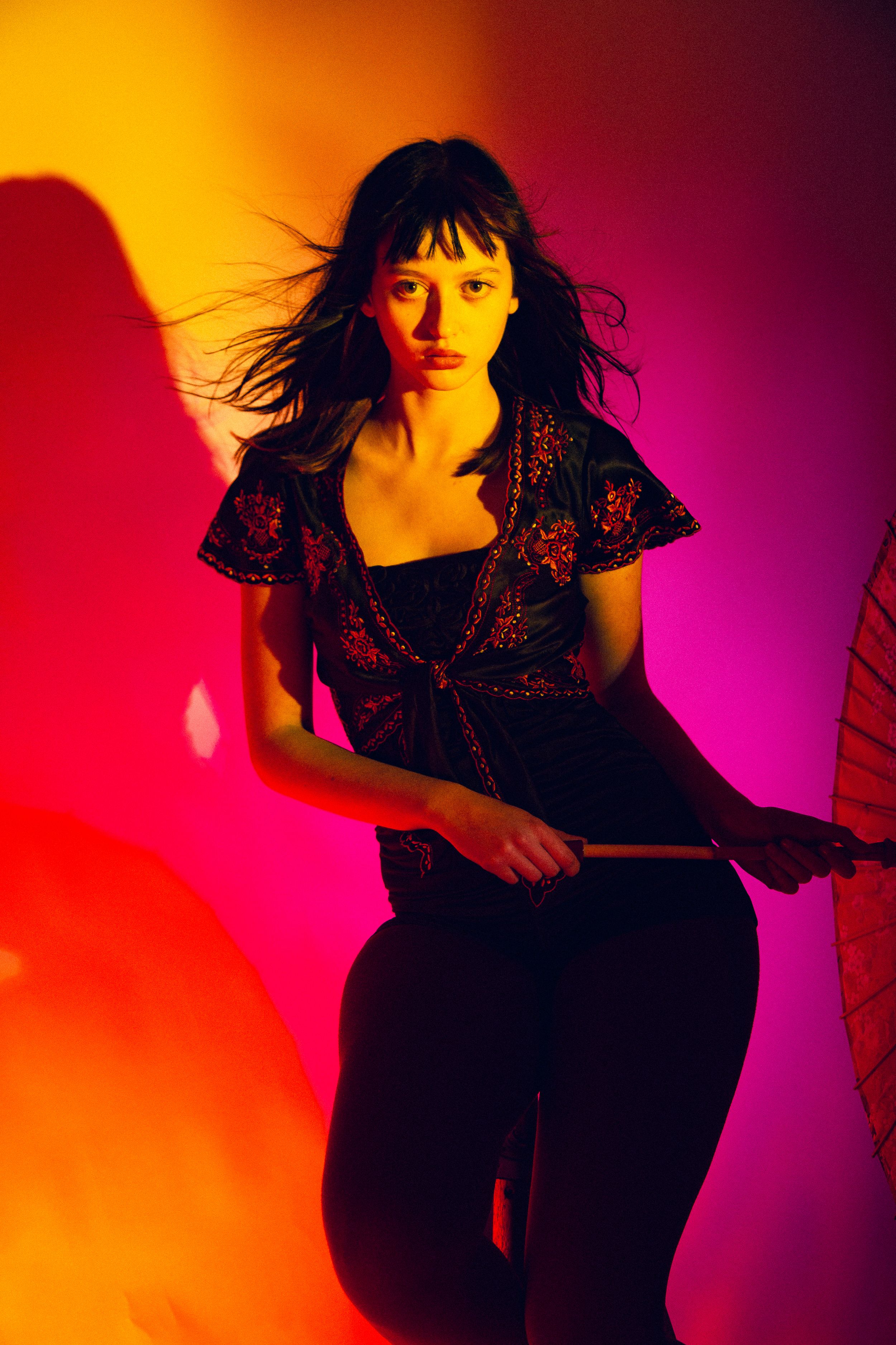 A silhouette of a person in black dress dancing against vibrant orange and purple gradient lighting.