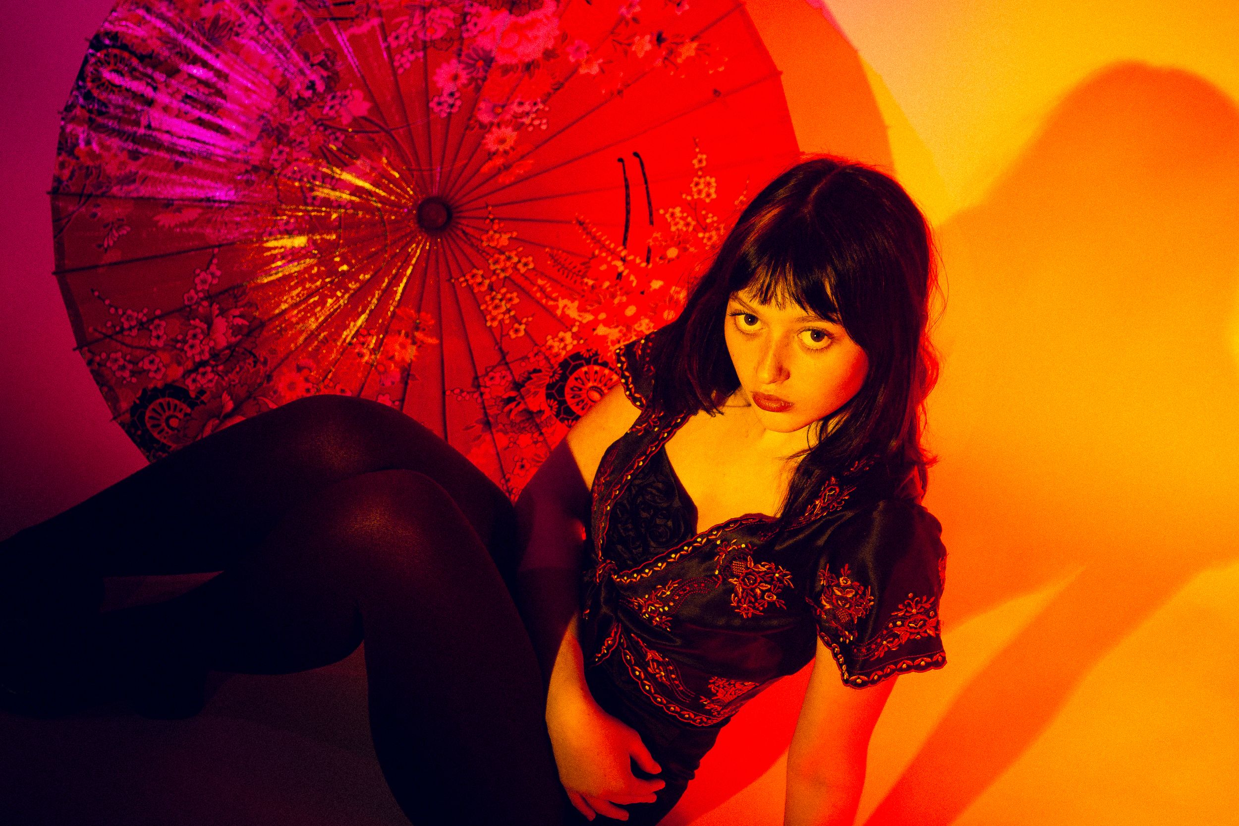 Silhouettes of figures with parasols against vibrant orange and red background create a dramatic Asian-inspired scene.