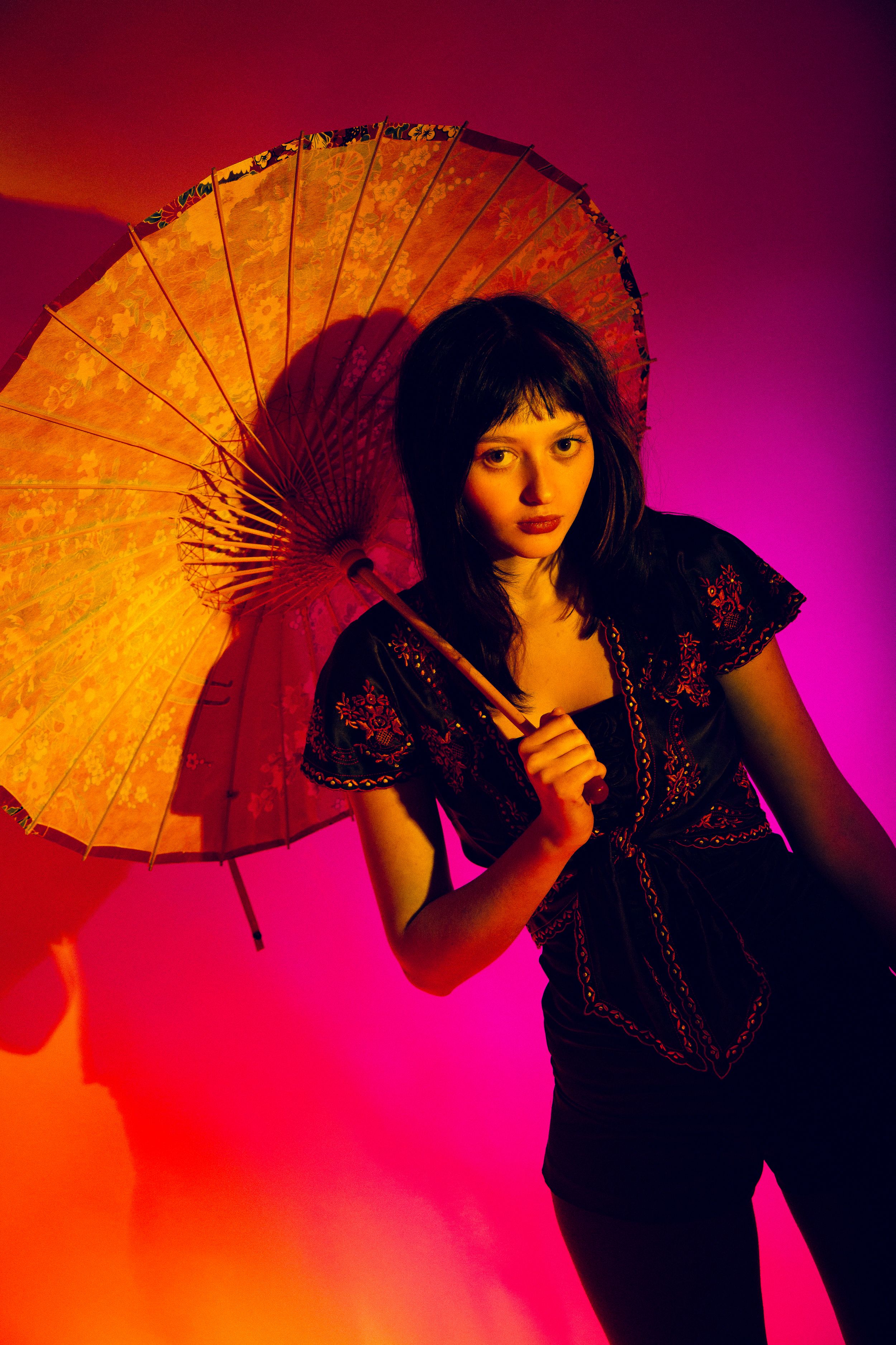 A silhouette poses with a decorative parasol against a vibrant red and purple backdrop in a dramatic fashion series.
