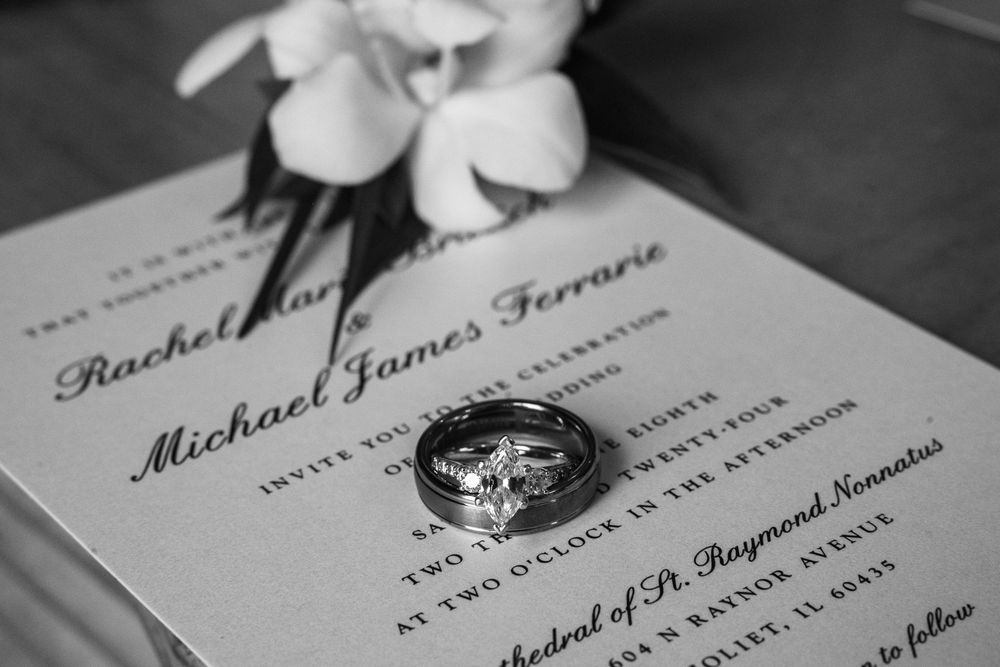 Black and white wedding invitation details with elegant calligraphy text and rings on display.