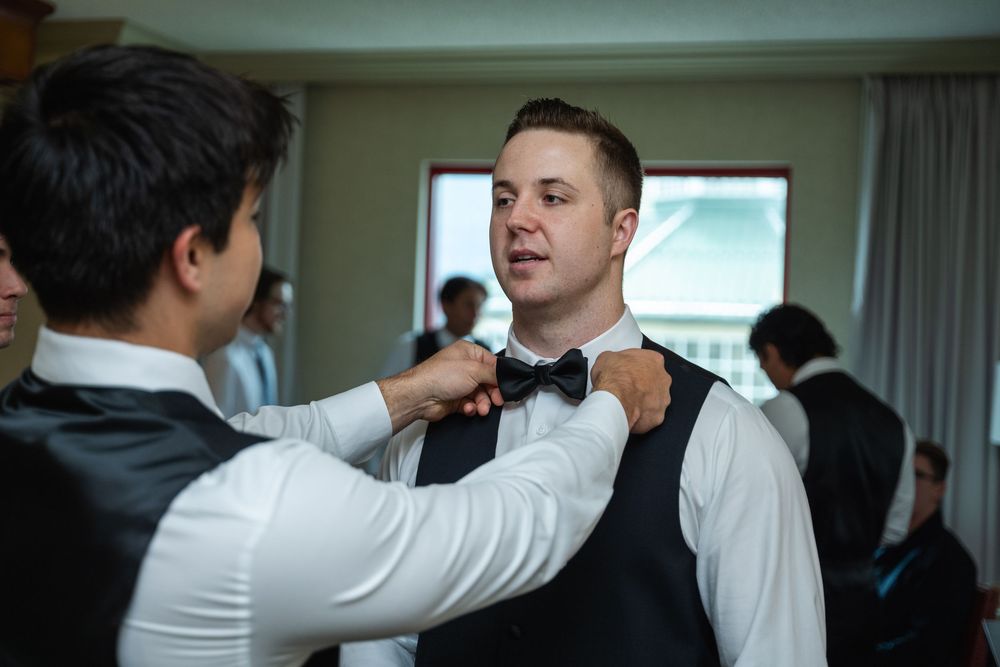 A person helps another adjust their tie and collar while getting dressed in formal attire.