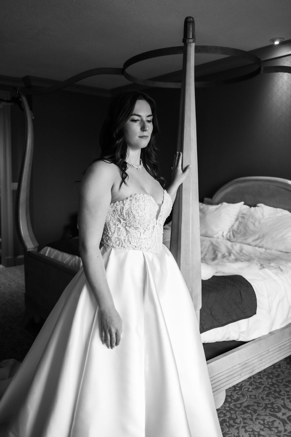 A bride in a flowing white wedding gown poses in a hotel room with elegant lighting and decor.