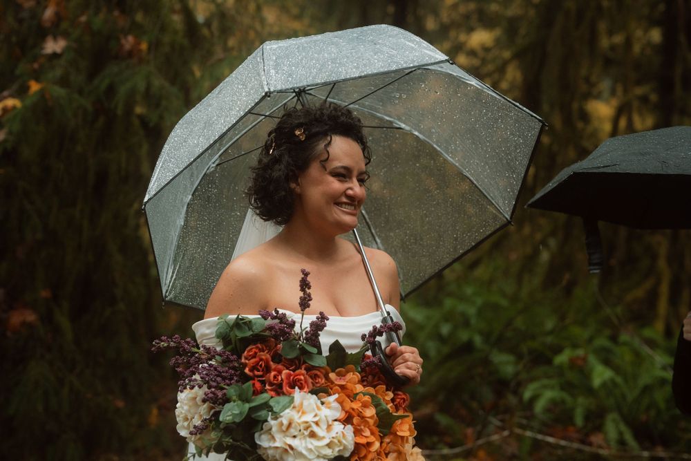 A joyful moment with beautiful autumn-colored wedding bouquet under a clear umbrella in the forest.