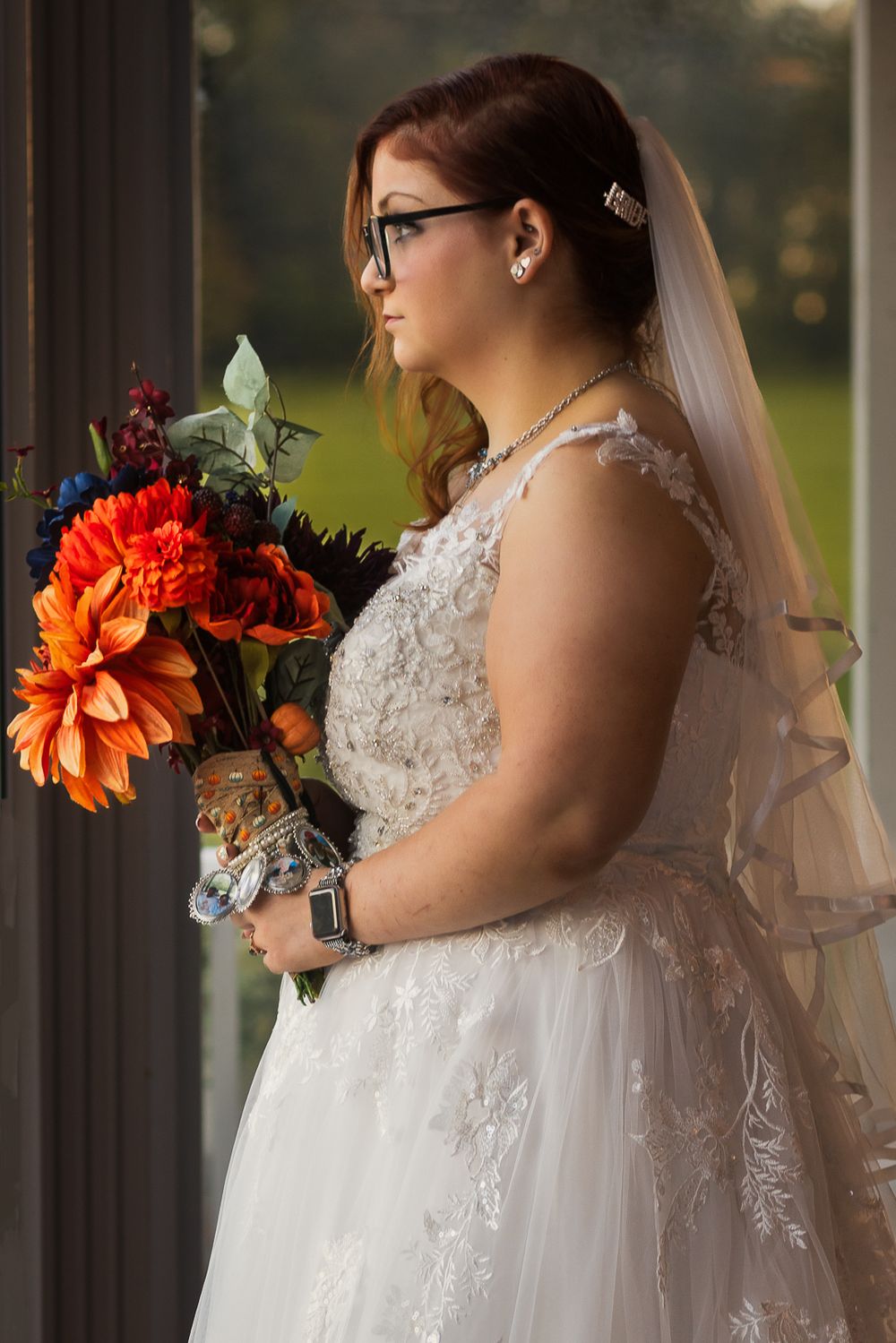 A bride in a lace wedding gown holds vibrant orange and red flowers against a dark background.