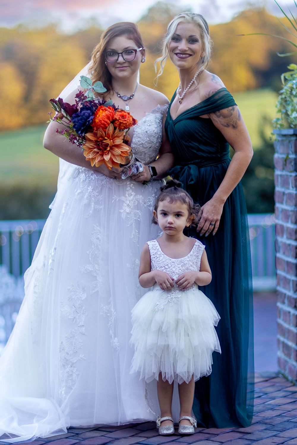 Wedding party members in formal attire posing together on a brick patio during autumn.