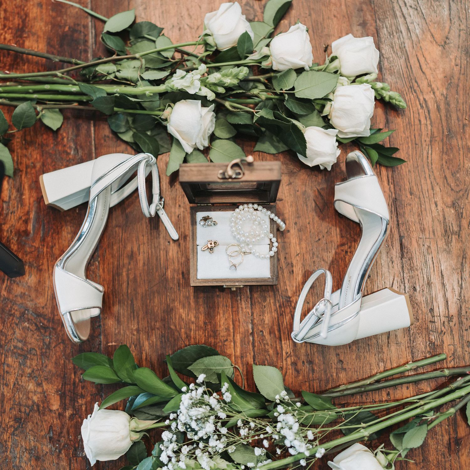 White roses and baby's breath flowers with green foliage arranged on a rustic wooden surface with ribbon accents.