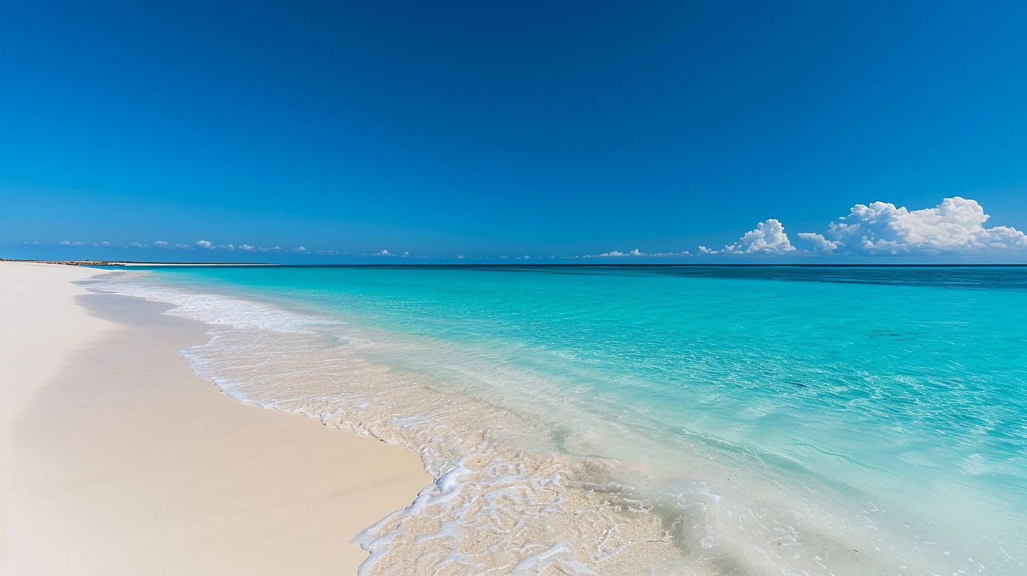 Pristine turquoise ocean waters meet white sandy beach under bright blue sky with fluffy clouds on tropical coastline.