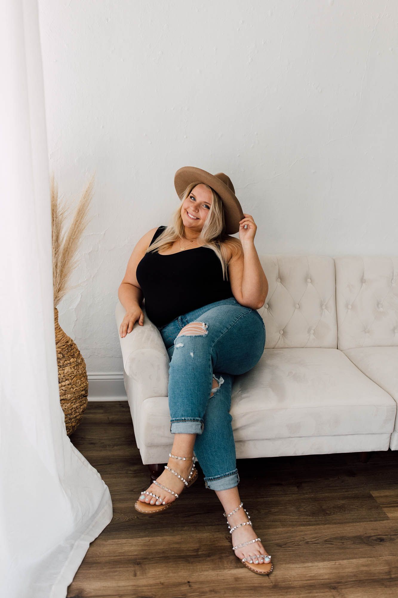 Casual indoor photoshoot on white couch wearing denim and sandals in natural light.