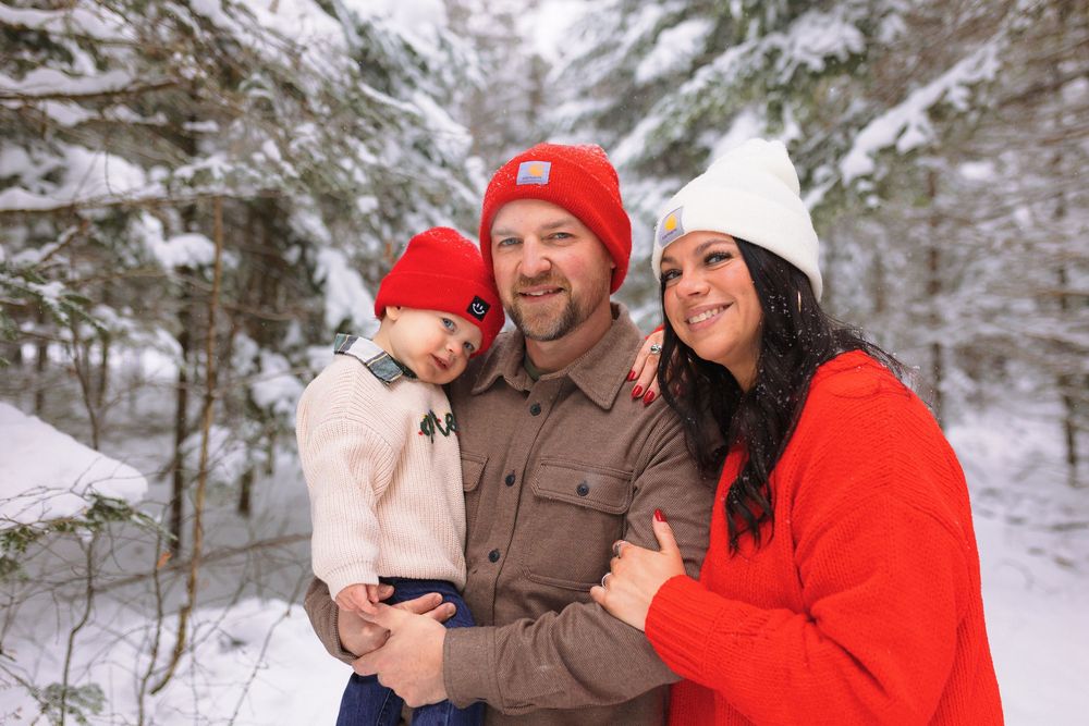 Family wearing winter coats shares joyful moments together in a snowy forest setting.