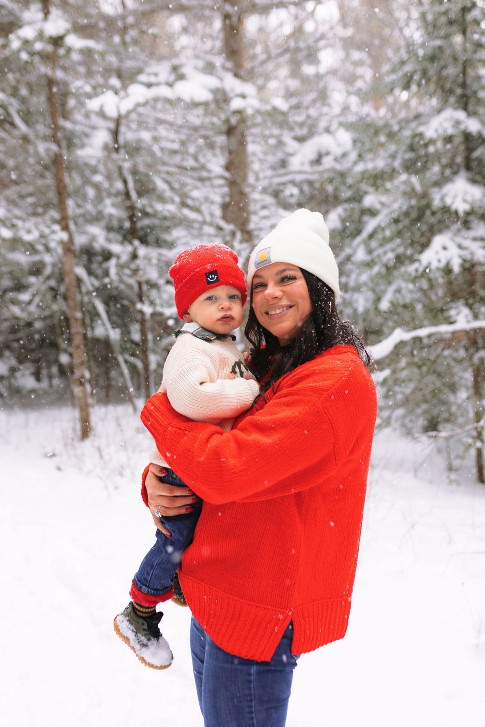 A parent and child share joyful moments together in a snowy winter forest while wearing red sweaters.