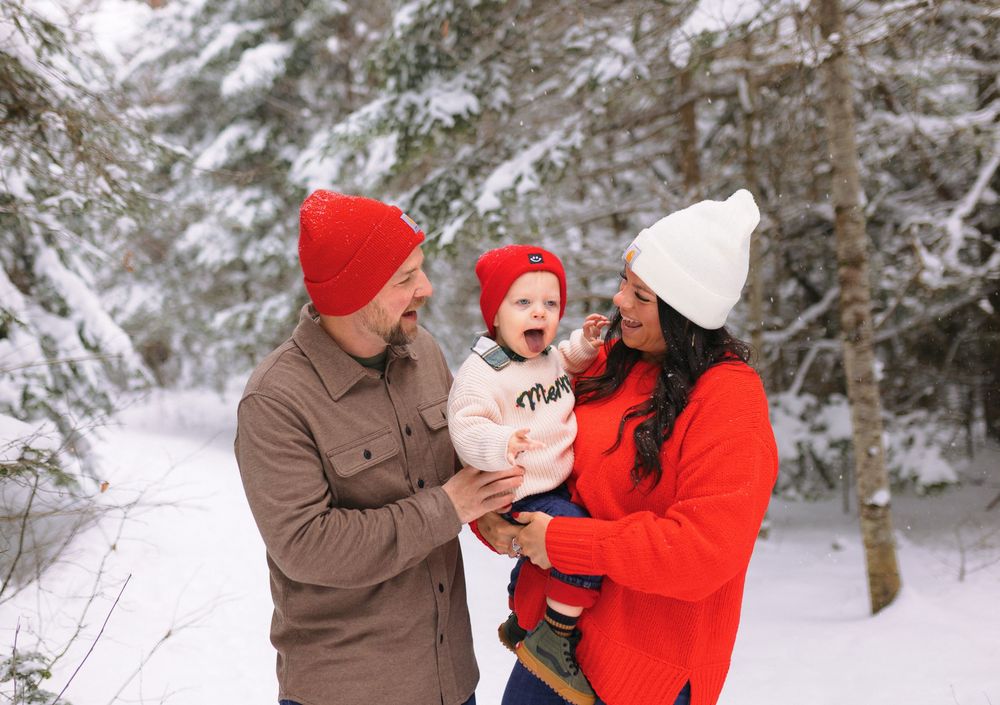 A family enjoys a winter moment together in a snowy forest setting wearing cozy winter hats and jackets.