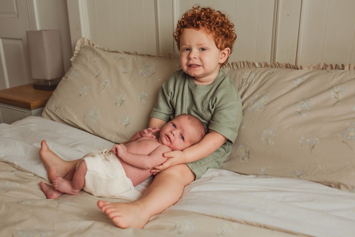 Two siblings share a sweet moment together on a beige couch, with one wearing a sage green shirt.