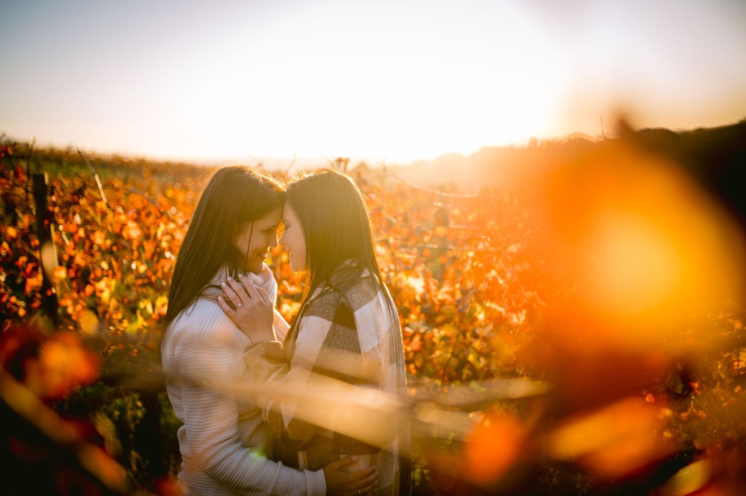A romantic couple embraces in a sunlit field of wildflowers during golden hour sunset.