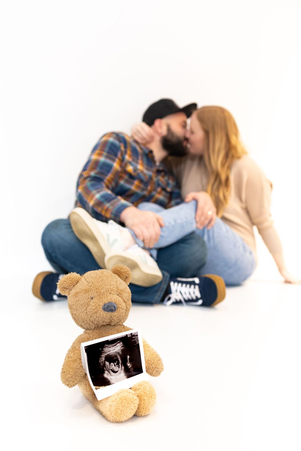 A pregnancy announcement photo series shows a couple laying with a teddy bear holding an ultrasound photo.