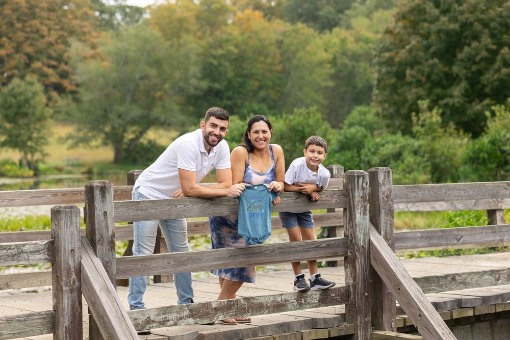 A couple sits together on a rustic wooden bridge surrounded by lush greenery on a sunny day.
