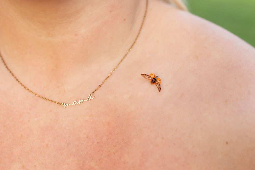 A delicate gold chain necklace with small beads lies against a soft pink background.