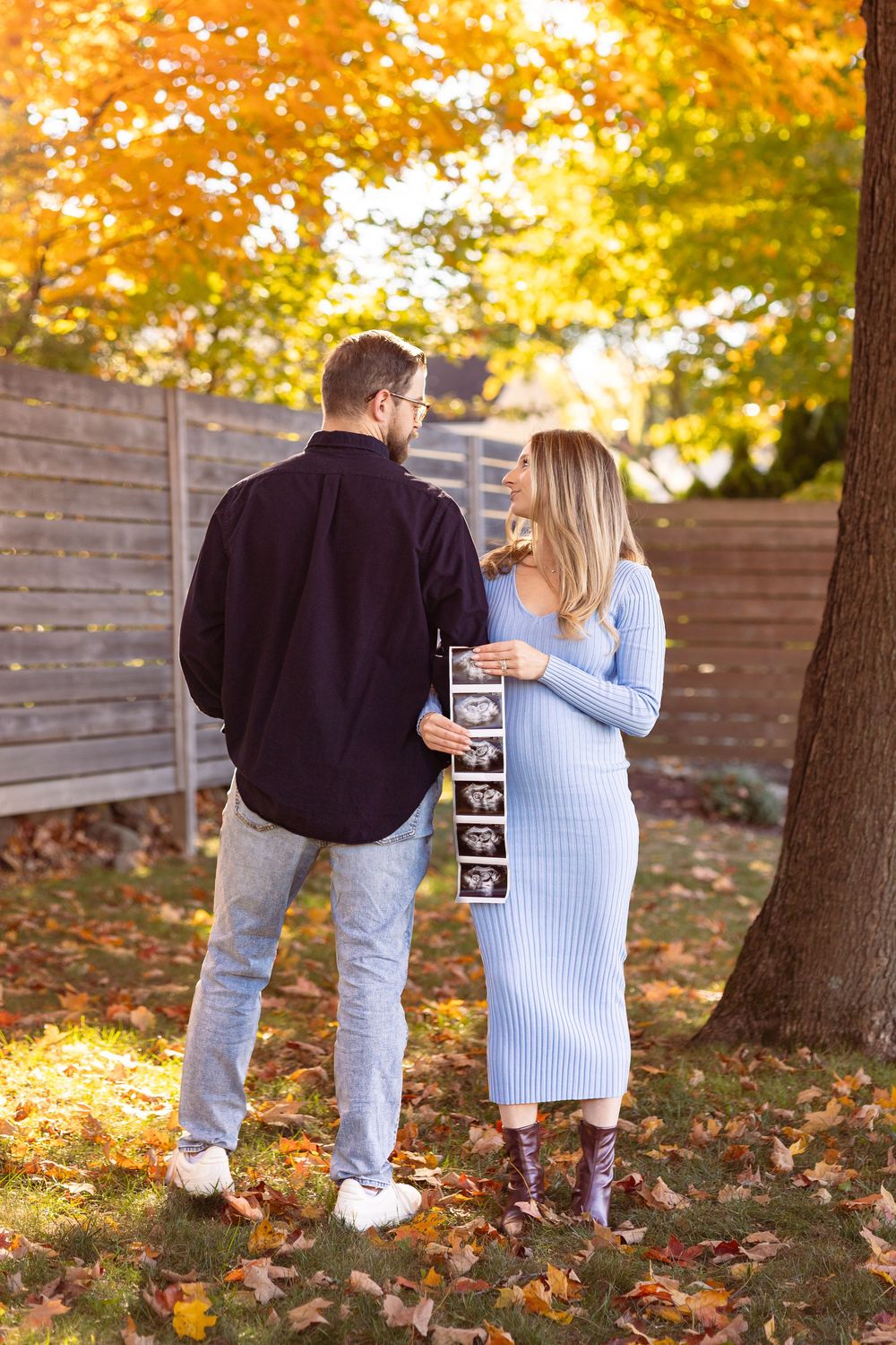 A couple walks together through autumn leaves during a fall photo session in a park.