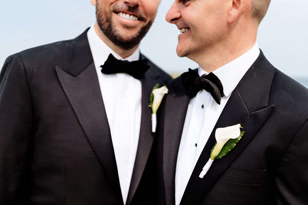 A group of groomsmen in black tuxedos with white boutonnieres smile and laugh together at a formal event.