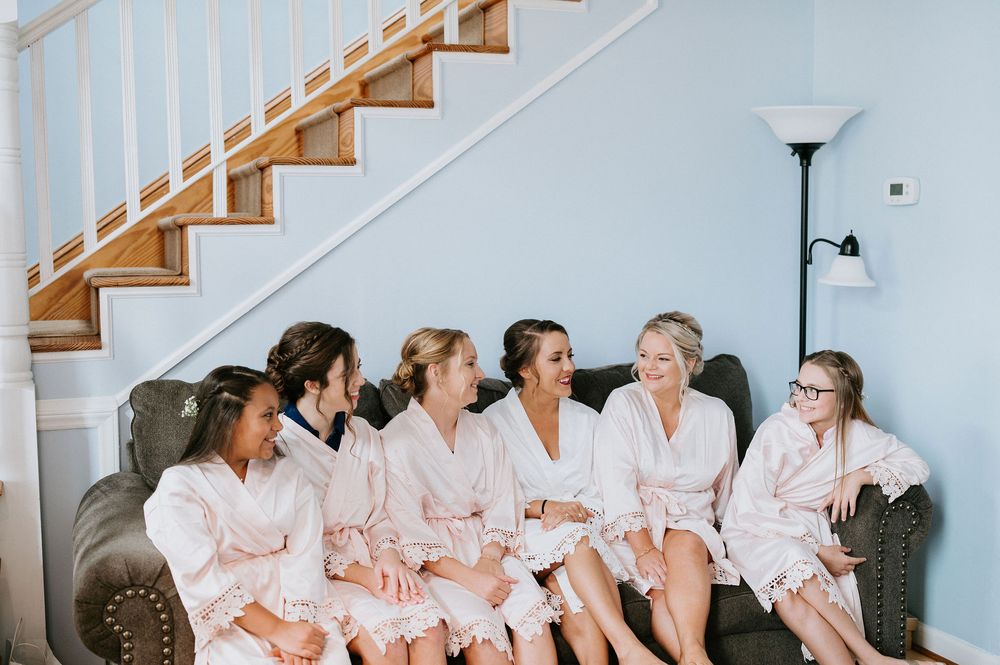 Row of bridesmaids in pink robes sitting on stairs during wedding preparations.