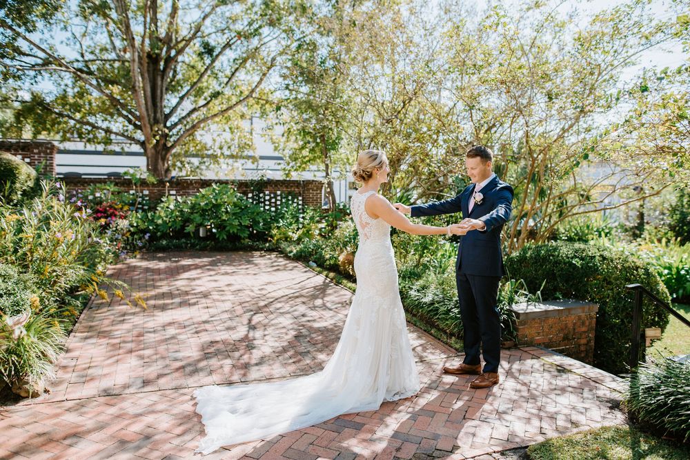 A couple shares a romantic moment in a lush garden setting with dappled sunlight filtering through the trees.