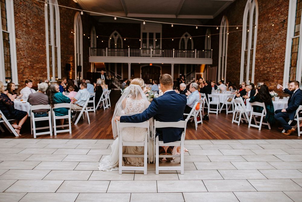Wedding reception venue setup with white chairs and brick walls in an indoor space.
