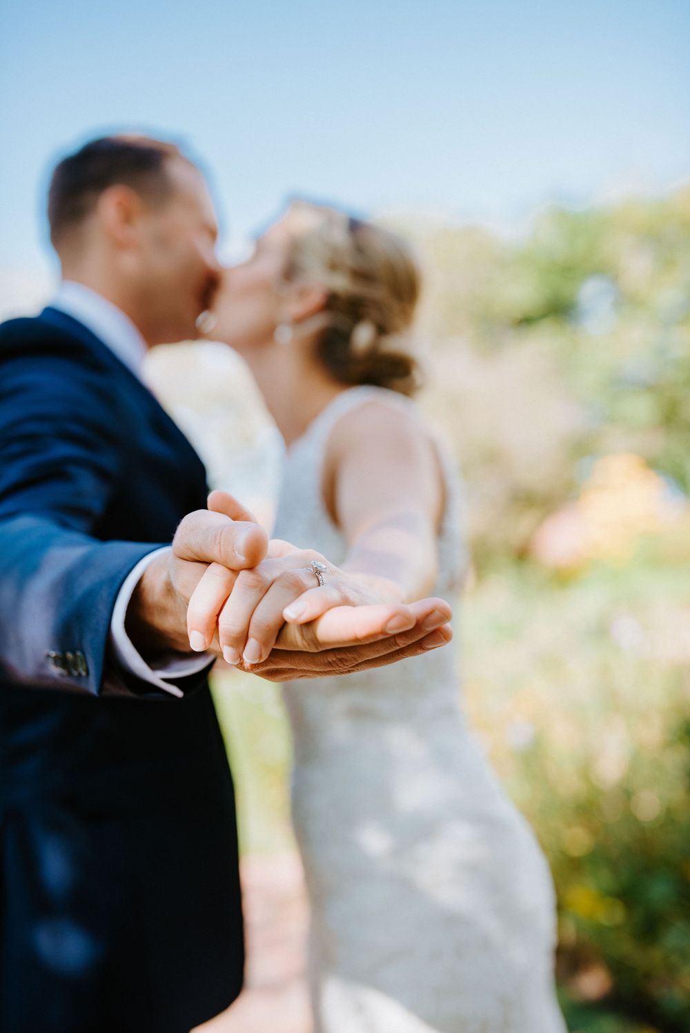 A couple shares a romantic kiss while holding hands in a garden setting during their wedding day.