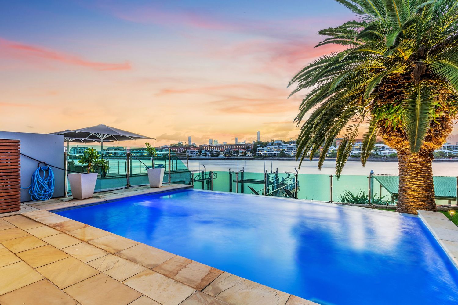 Stunning waterfront pool with palm tree and panoramic harbor views at sunset.