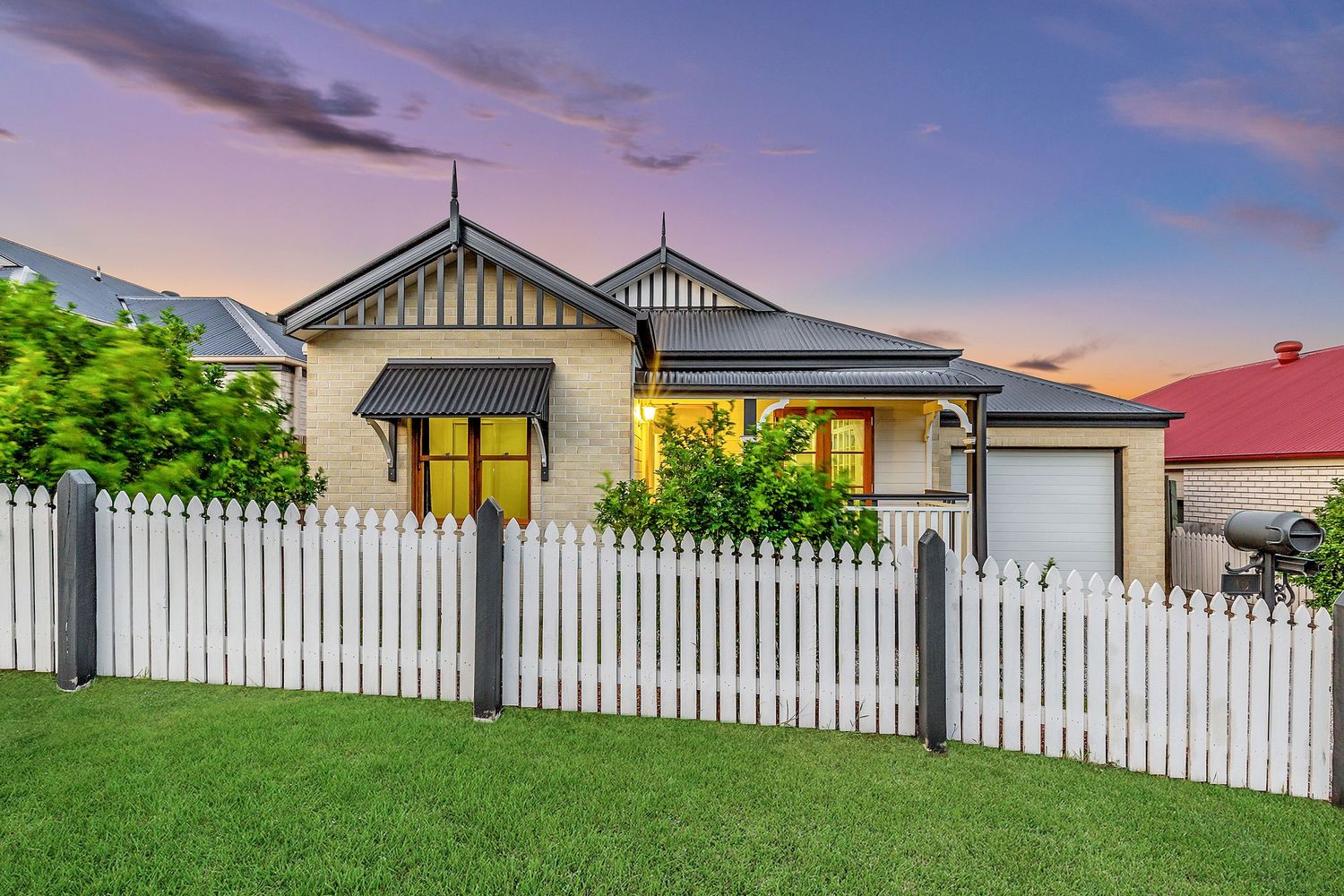 Charming heritage home with white picket fence, decorative gables, and lush lawn.