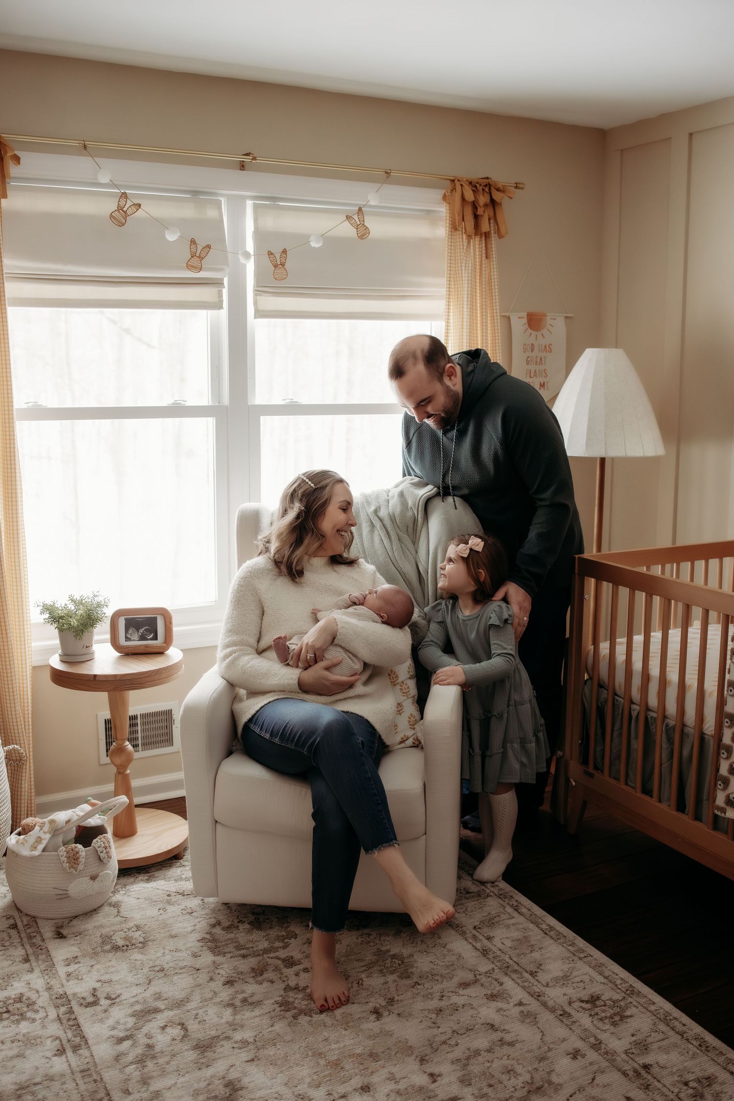A cozy nursery room scene with a white armchair, wooden crib, and soft area rug in natural lighting.